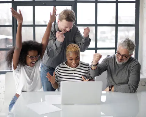 A small team cheering a win around a laptop